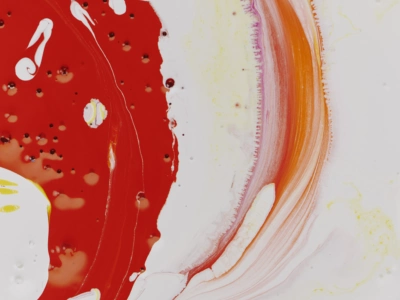 Close up image of red and yellow paint pigments swirled over white paint