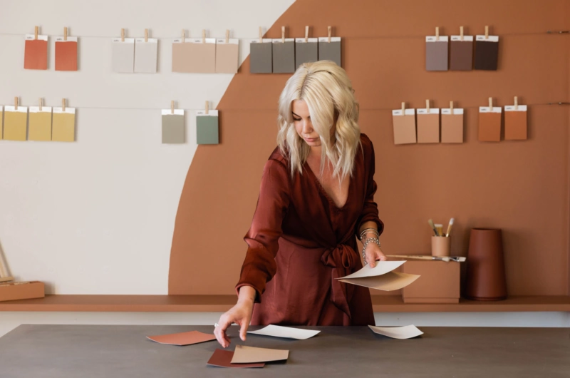 A lady creating a colour scheme with paint sample cards in front of an orange wall